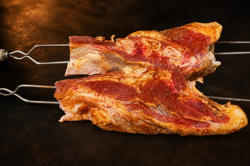 Peças de costela abertas e cobertas de dry rub, espetadas antes da brasa